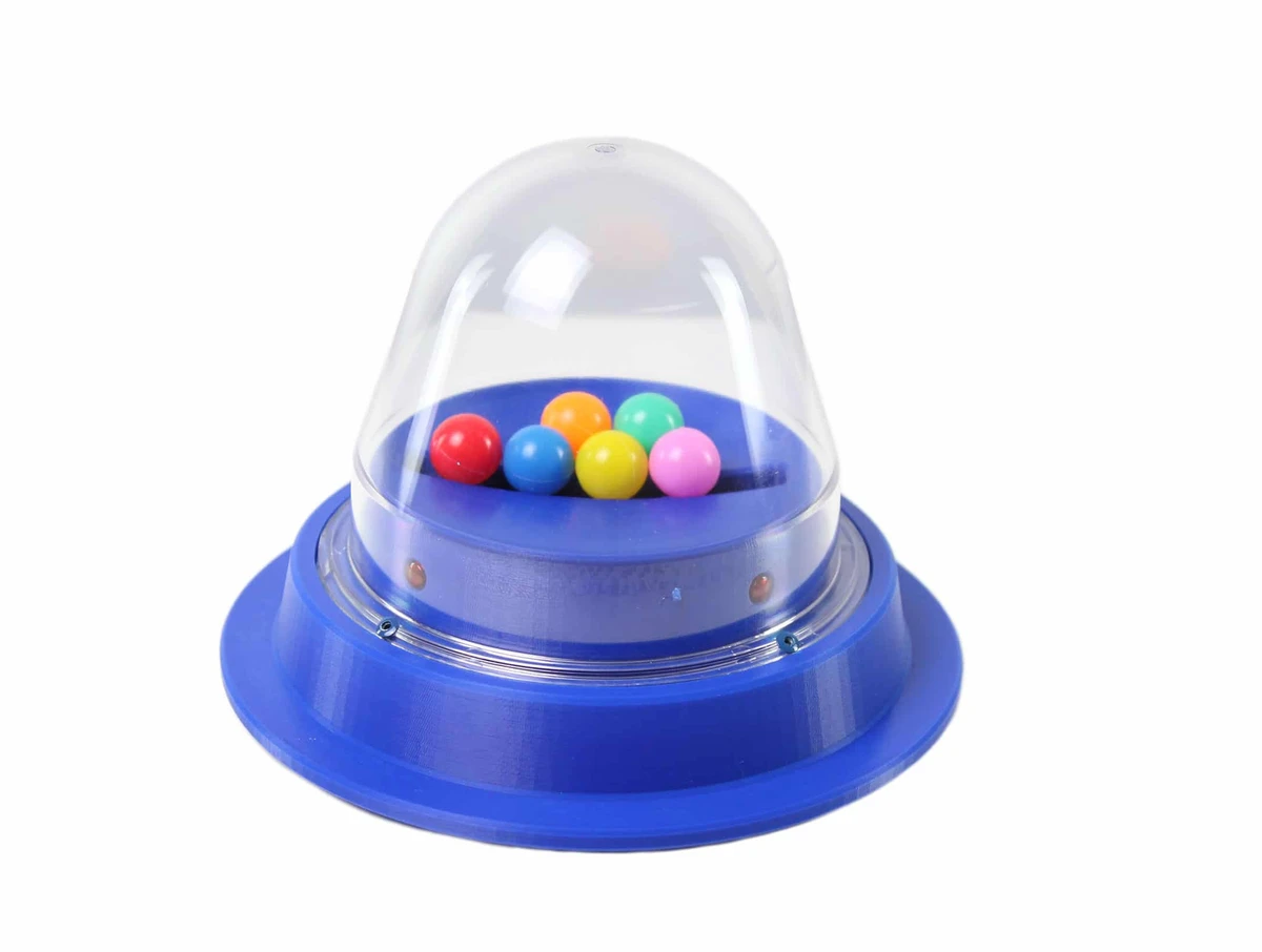 Un giocolo popper rotondo con cupola trasparente su base colorata, contenente palline piccole che rimbalzano all'interno della cupola quando attivato.