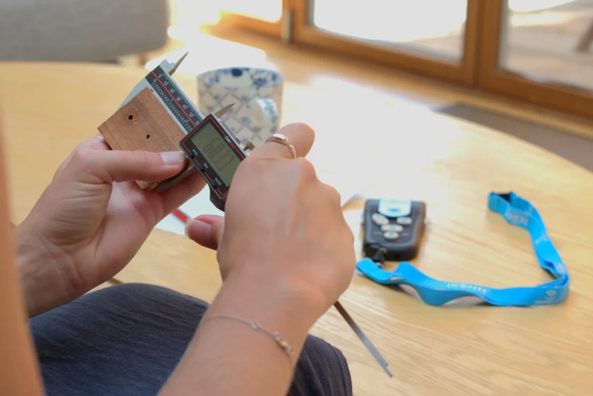 Hands measuring a small wooden plate with the CP-1, the Controller on the table behind