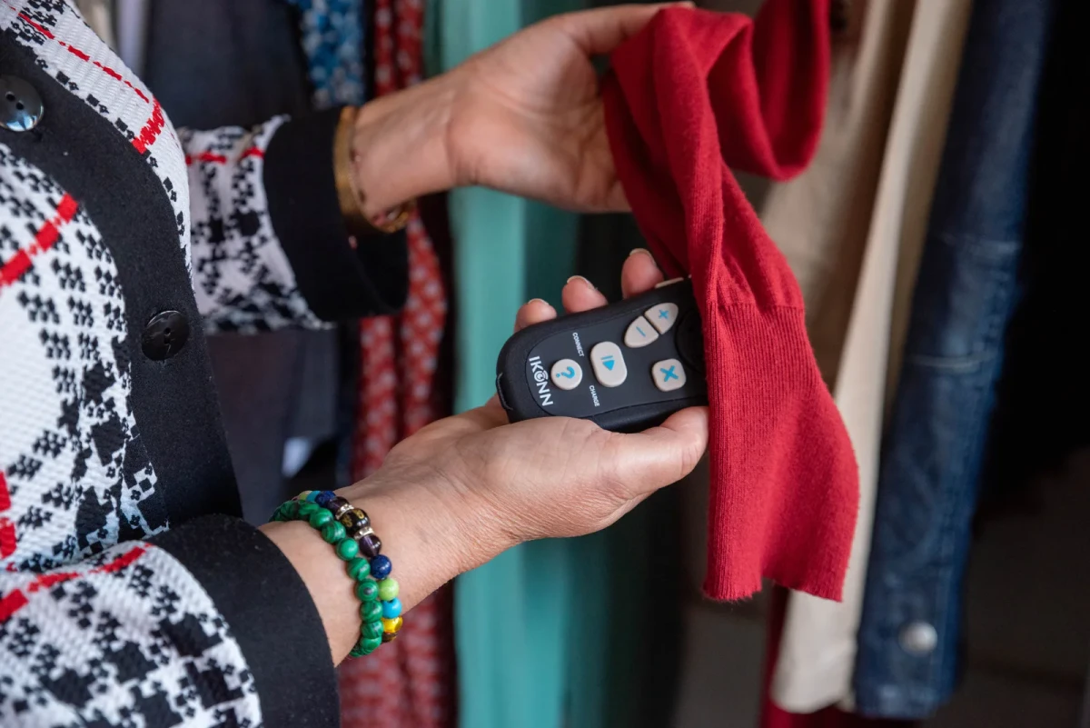 A woman at a wardrobe holding the Controller and CS-1 against a red cardigan sleeve