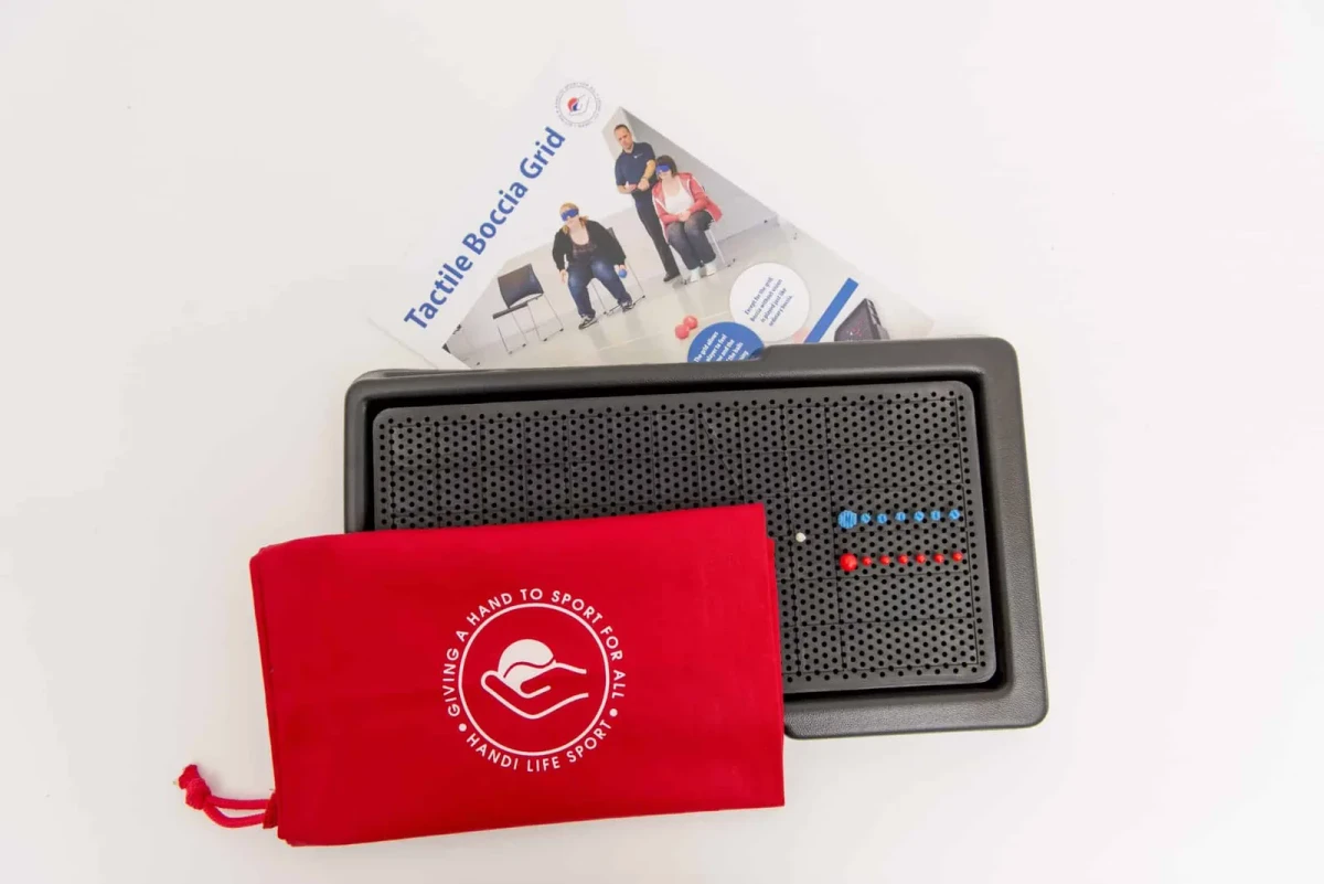 Black tactile boccia grid board with rows of small red and blue pegs and one white peg, plus a red storage pouch.