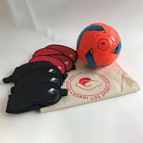 Ein orangefarbener Blindenfußball, ein Stapel rot-schwarzer Augenmasken und eine Baumwolltasche.