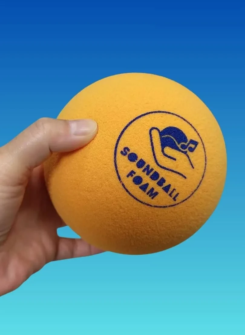 Una mano che tiene una palla sonora in schiuma arancione brillante con la scritta Soundball Foam