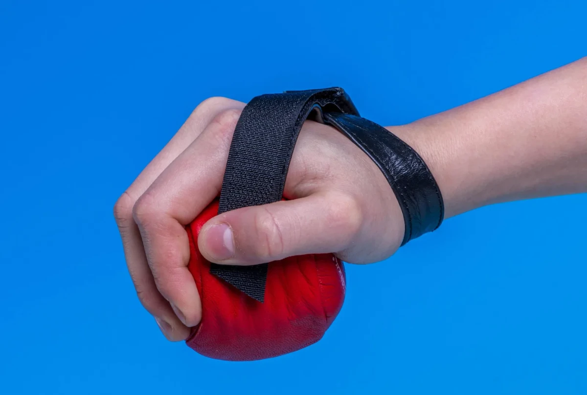 Una mano che impugna un peso da polso rosso Trimmy fissato con una fascia in velcro nera.