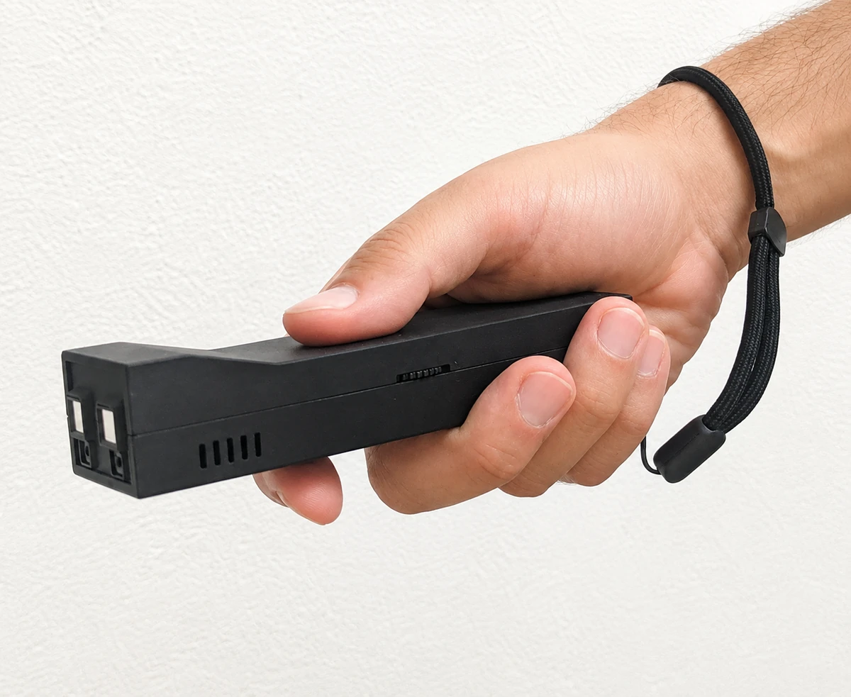 A hand holding the black Eye-pass device like a torch, with its wrist strap around the wrist.