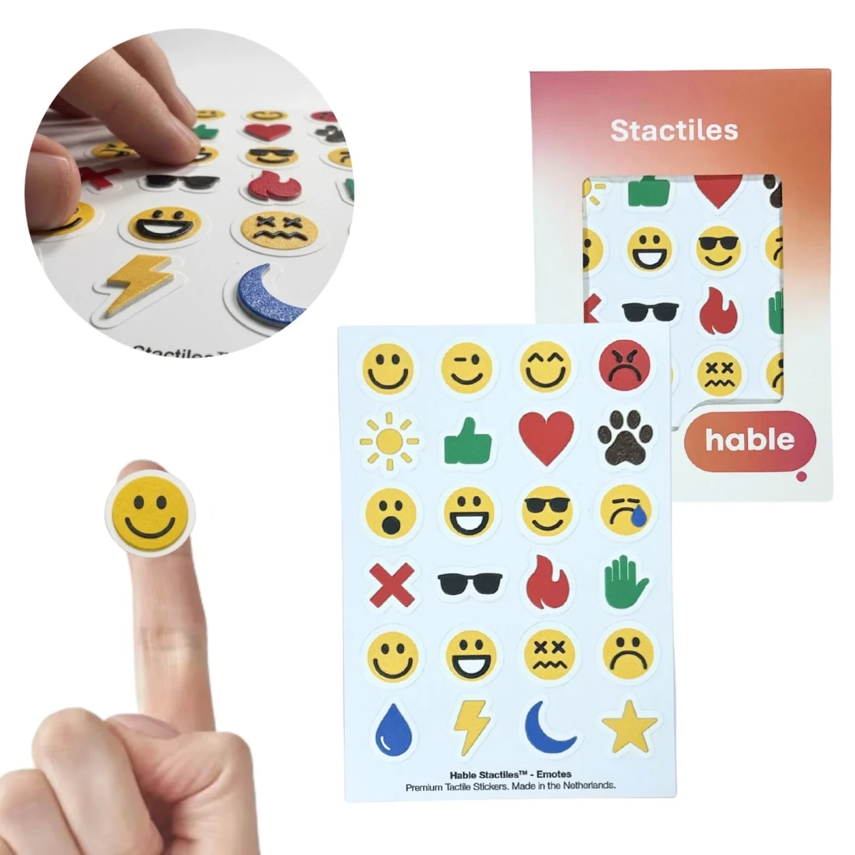 Il set Hable Stactiles Emojis: un foglio bianco di adesivi emoji in rilievo che include faccine sorridenti, ammiccanti, sorprese, tristi e stordite, un sole, un pollice verde in su, un cuore rosso, un'impronta di zampa, occhiali da sole, una fiamma, una mano, una goccia d'acqua, un fulmine, una luna e una stella, mostrato con la sua scatola arancione. Un polpastrello tiene una singola faccina gialla sorridente e un riquadro mostra dita che toccano gli adesivi.