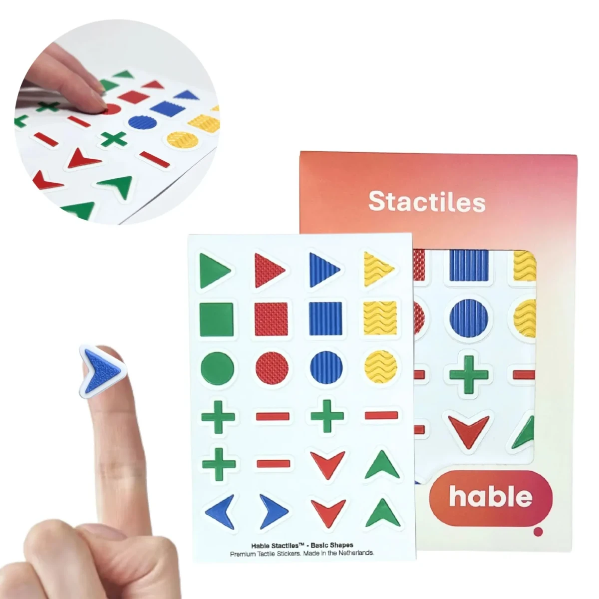 Il set di forme base Hable Stactiles: un foglio bianco con forme in rilievo in verde, rosso, blu e giallo, ciascuna con una texture superficiale diversa, tra cui triangoli, quadrati, cerchi, segni più e meno e frecce direzionali, mostrato con la sua scatola arancione. Un polpastrello tiene un singolo adesivo a freccia blu e un riquadro mostra dita che toccano le forme.