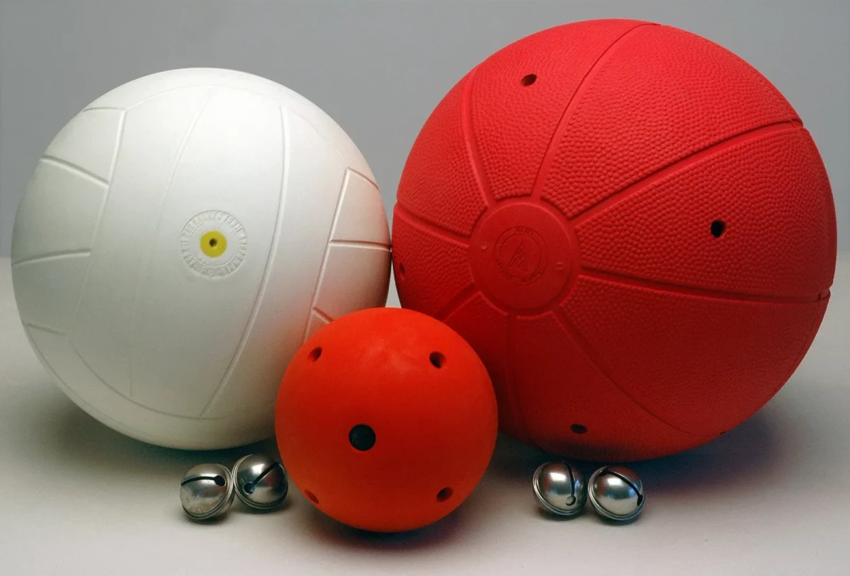 The WV bell ball range together: a football in the older white finish, a smaller red throwing ball with sound holes and a larger red goalball, with loose jingle bells.